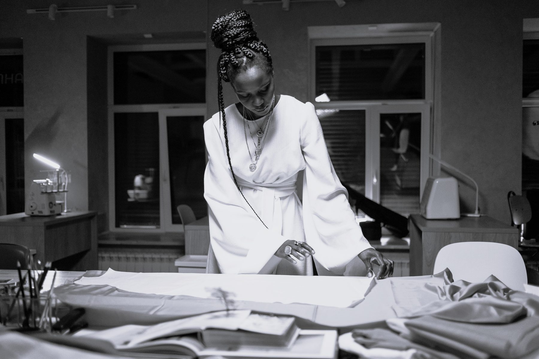 A designer in a white dress laying out fabric on her studio table, black and white