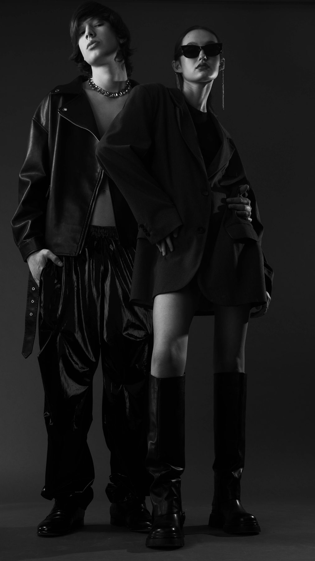 Two models in black leather and oversized tailoring, studio portrait in black and white